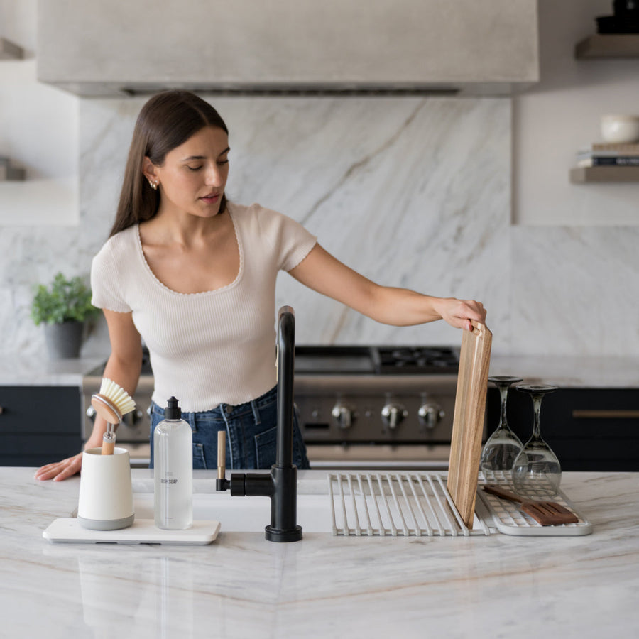 woman placing cutting board into slot of the over the sink dish pad, featuring brush holder and stone sink caddy