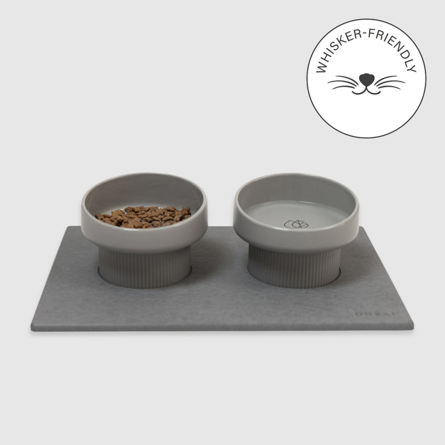 Two gray pet bowls with a mat on a white background, featuring a 'Whisker-Friendly' logo.