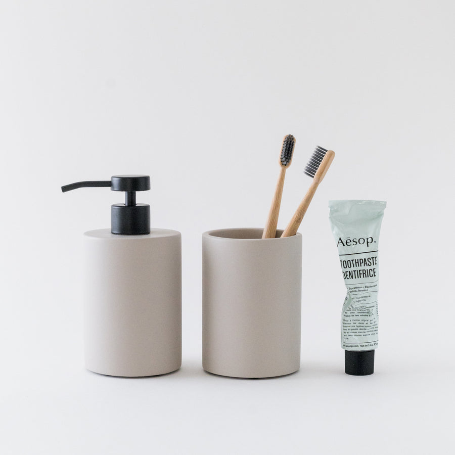 Bathroom essentials including a soap dispenser, toothbrush holder with toothbrushes, and Aesop toothpaste on a white background.
