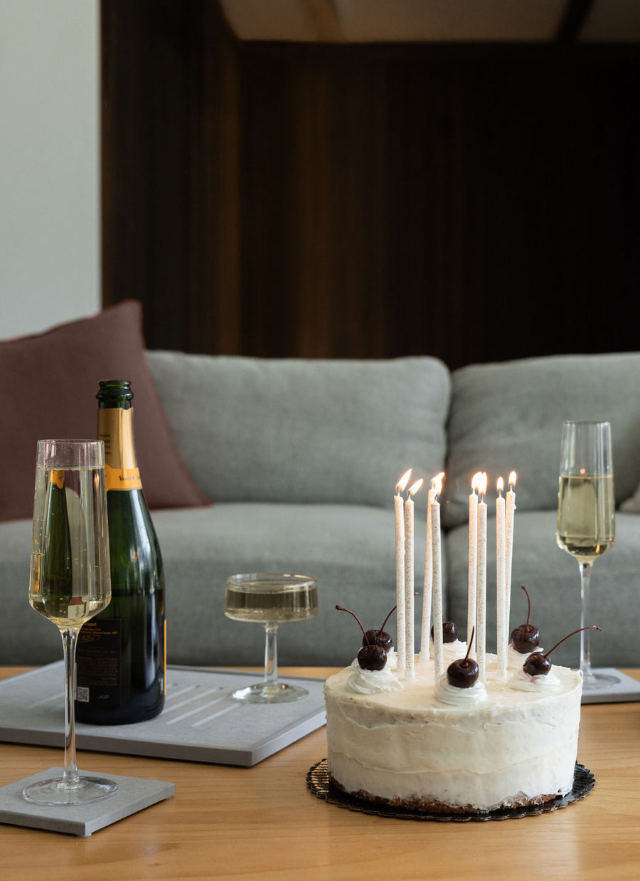 Birthday cake with lit candles, champagne bottle, and glasses on a table.