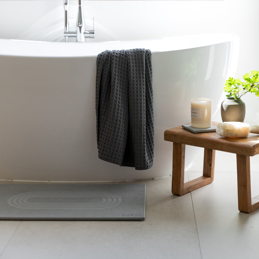 Bathroom setting with a bathtub, bath stone, towel, candle, and plant.

