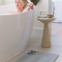 Woman relaxing in a bathtub with a small table next to her holding a glass of water and a bowl.