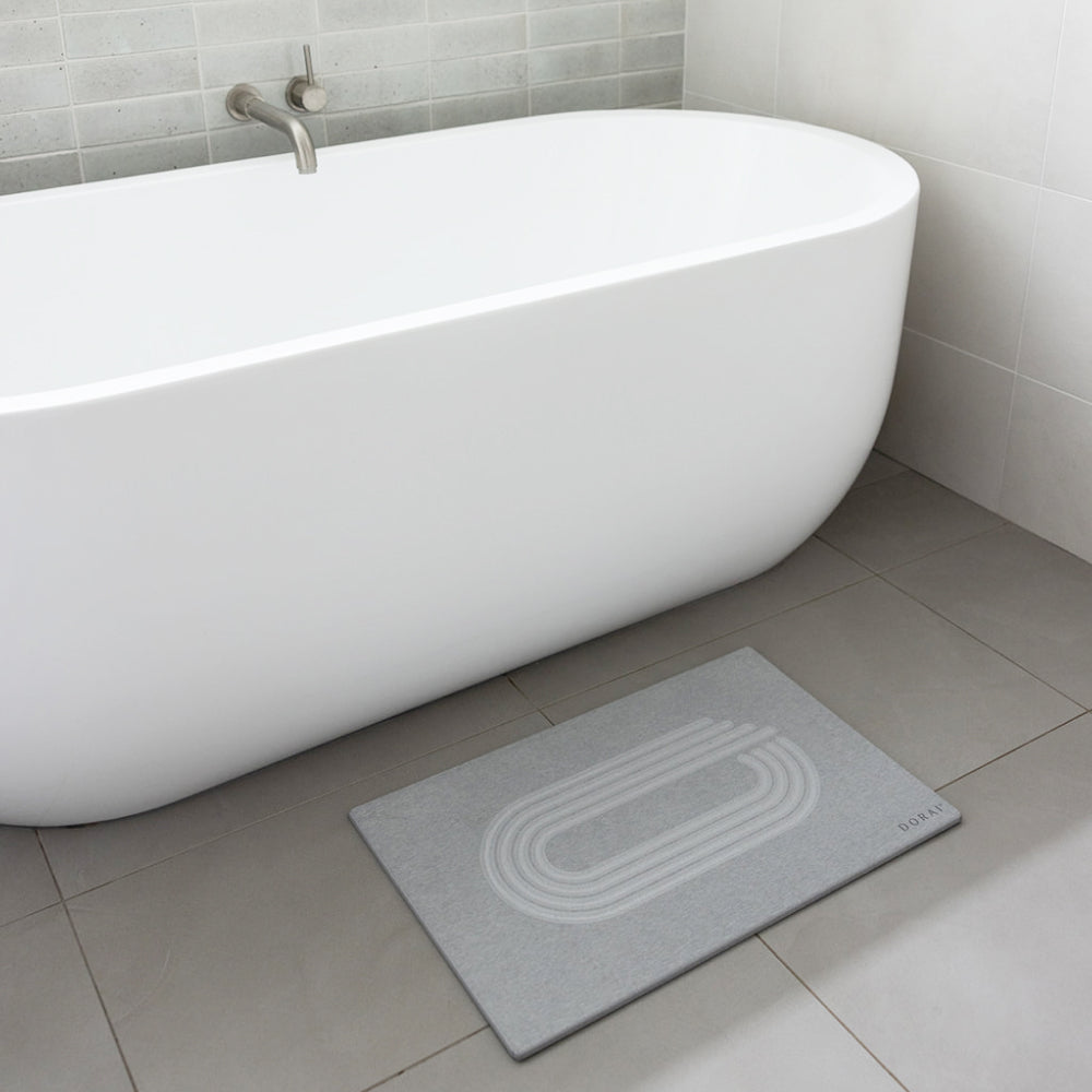 Gray bath mat in front of a white freestanding bathtub in a bathroom.
