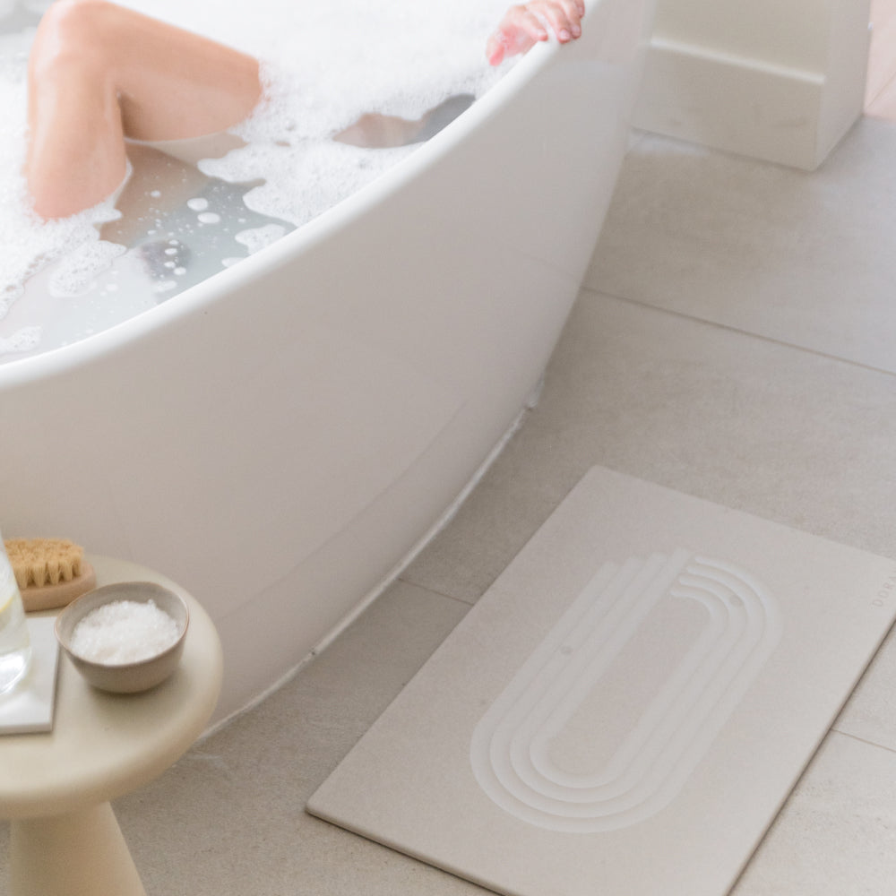 Person in a bathtub with a bath mat on the floor next to it