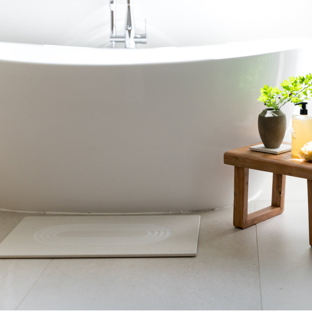 Bathroom with a large white bathtub and a wooden side table with decorative items and bath stone mat