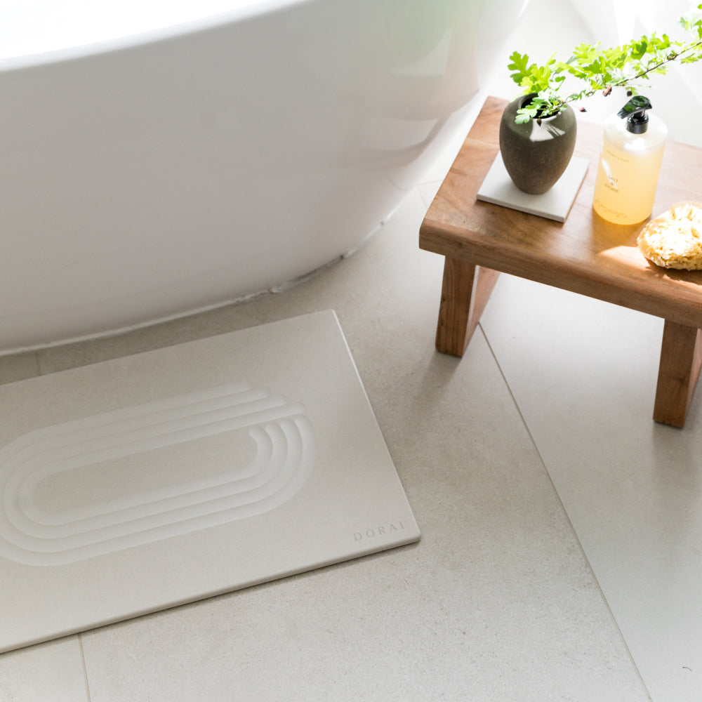 White bath mat on a bathroom floor next to a wooden table with decorative items.