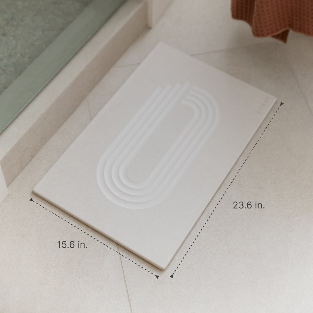 White rectangular bath mat with measurements on a tiled floor