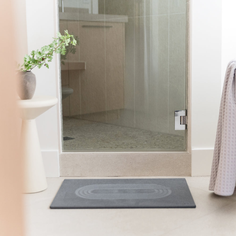 Bathroom with a glass shower and a gray mat on the floor.