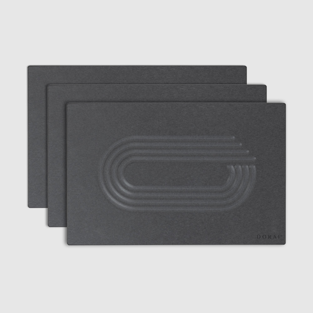 Three dark grey bath stones with embossed design on a light gray background