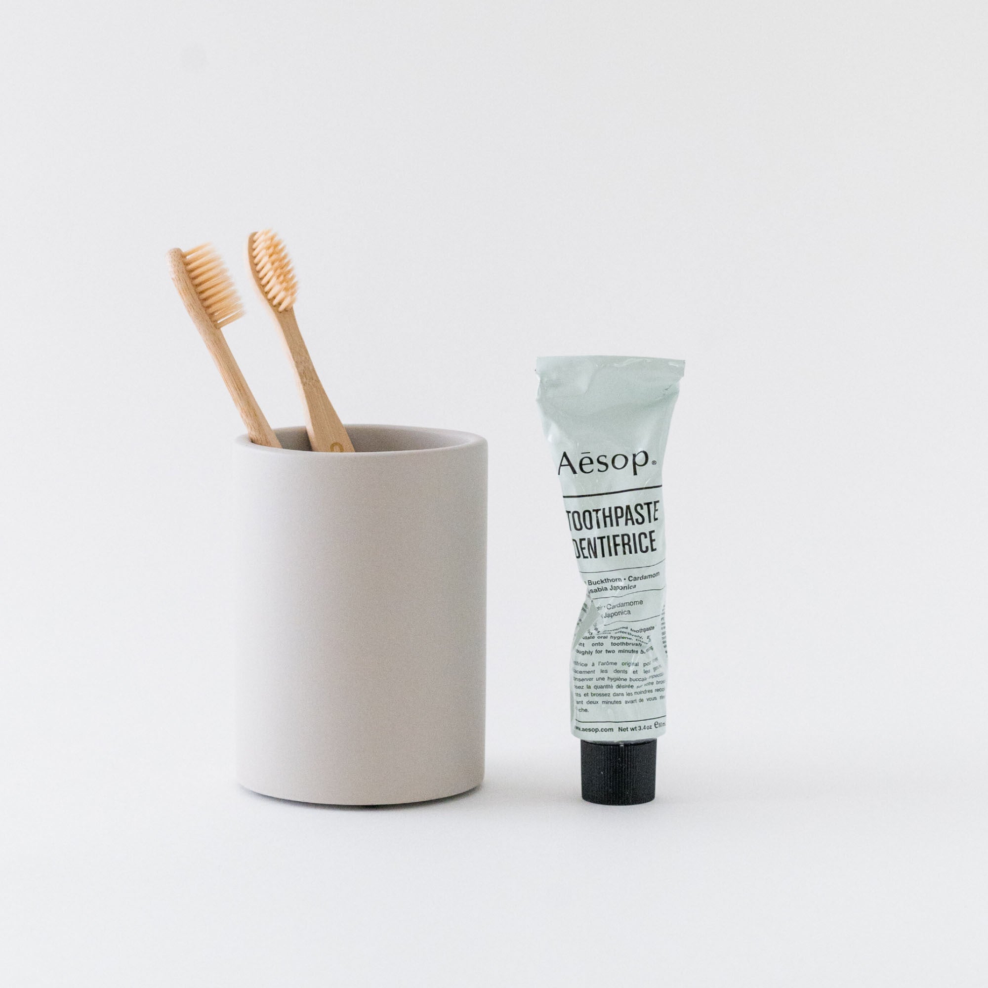 Concrete Brush Holder in Grey with toothbrushes next to toothpaste. 