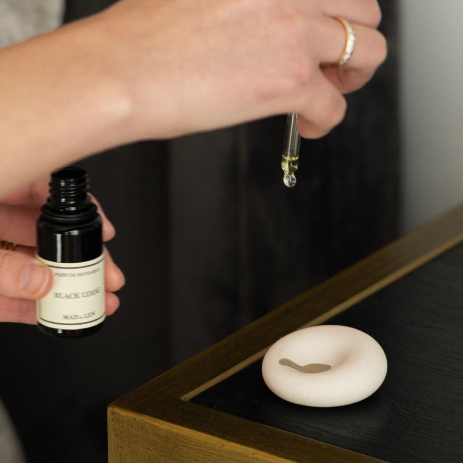 Person holding a dropper and bottle over a scent diffuser stone with a dark background