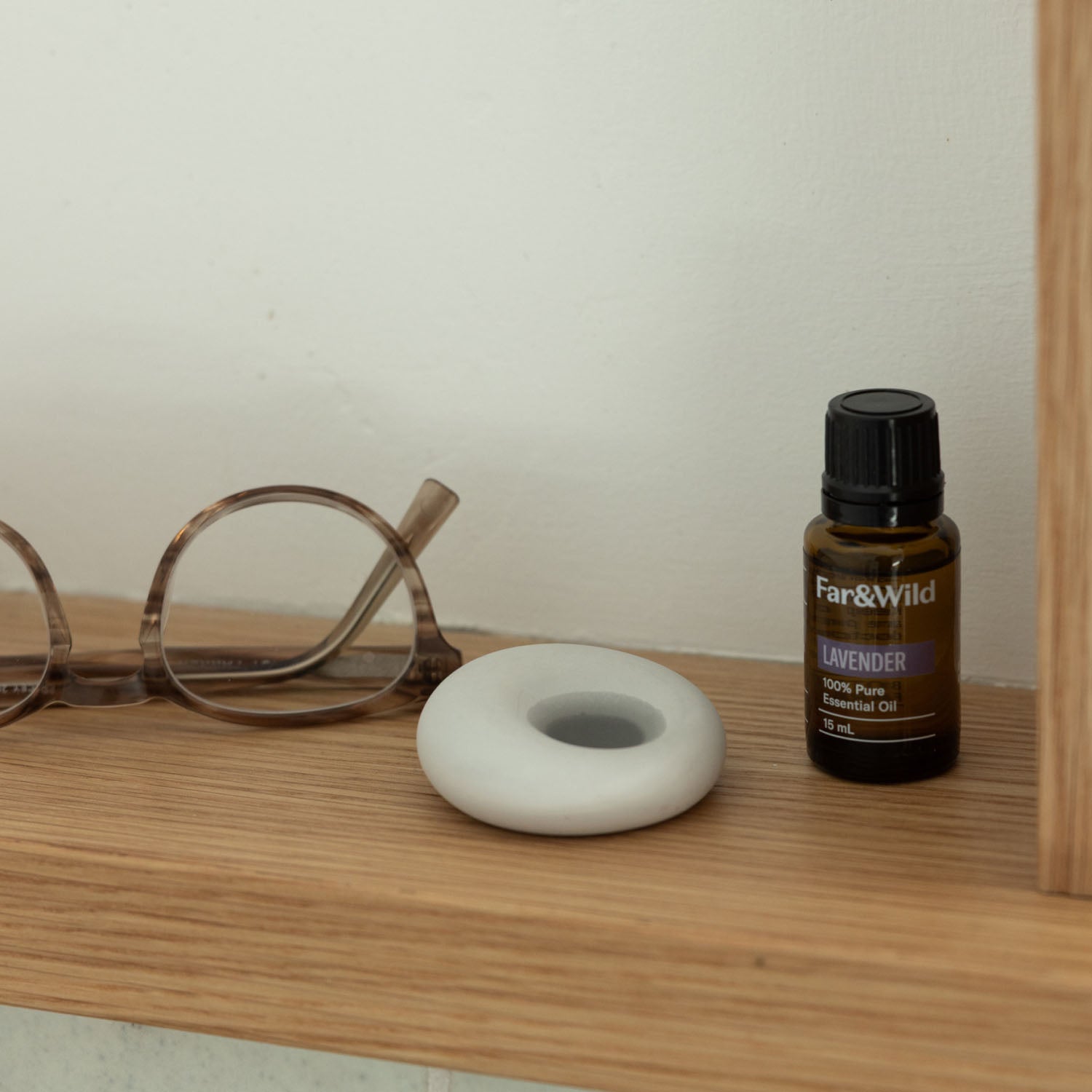 Scent stone next to essential oil  dropper on a wooden surface next to pair of glasses 