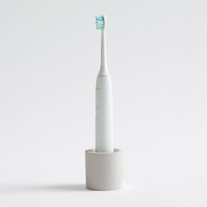 Electric toothbrush in a Soft Beige, stone toothbrush holder on a light gray background