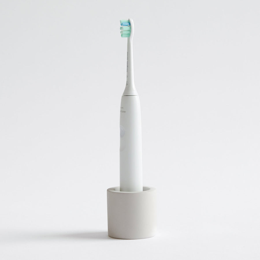 Electric toothbrush in a Soft Beige, stone toothbrush holder on a light gray background