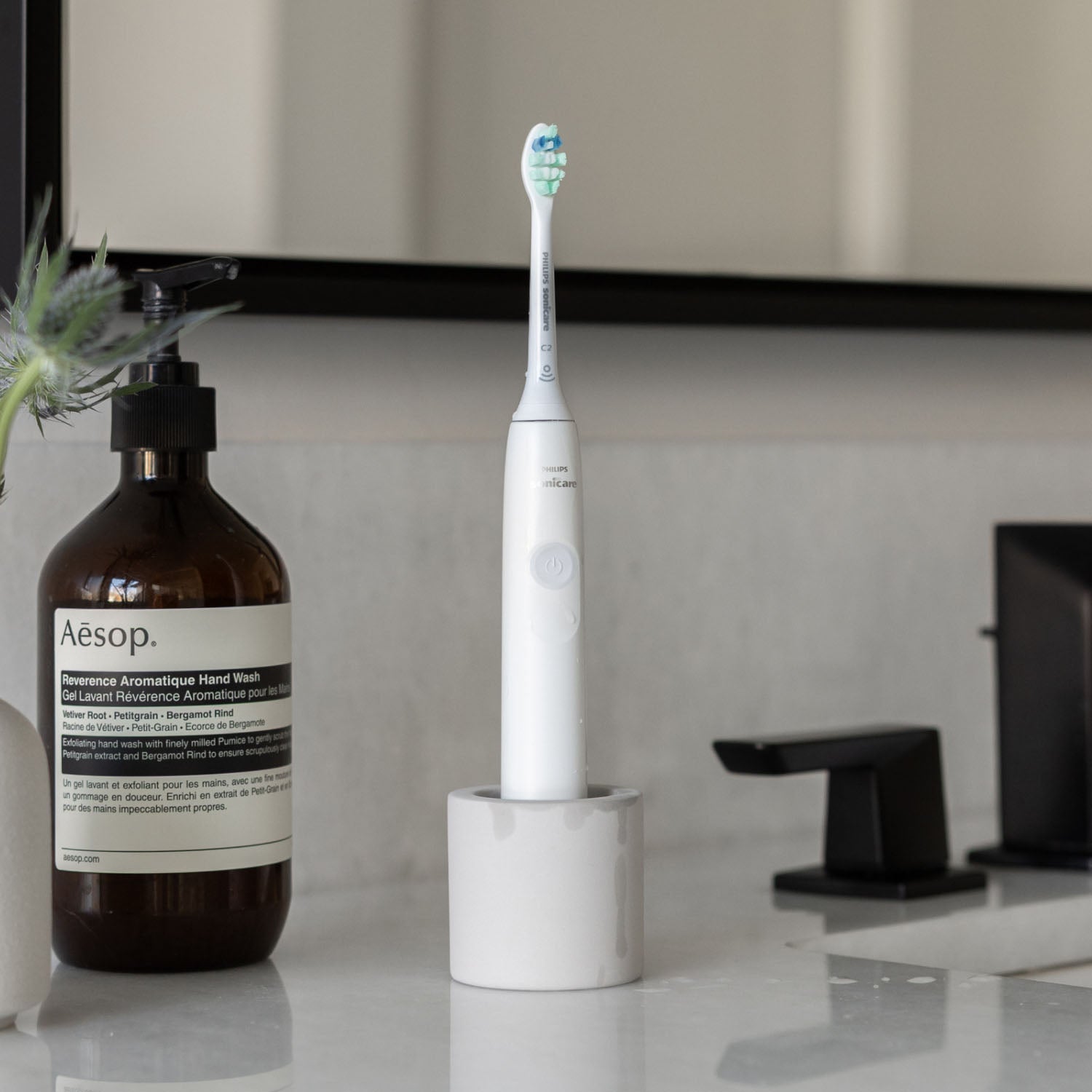 Electric toothbrush in a stone toothbrush holder on a counter next to a bathroom sink.