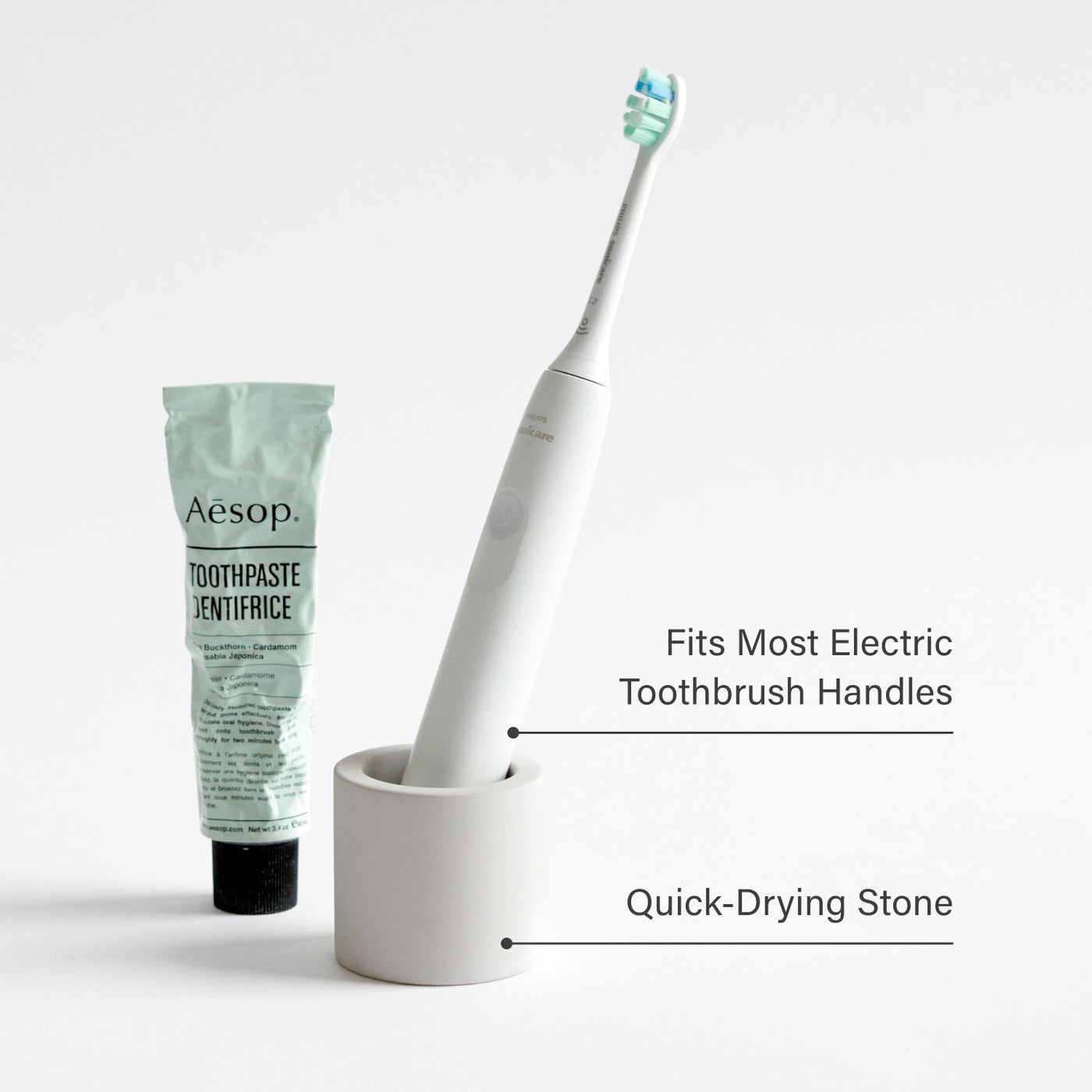 Electric toothbrush in a stone toothbrush holder next to toothpaste with product feature text