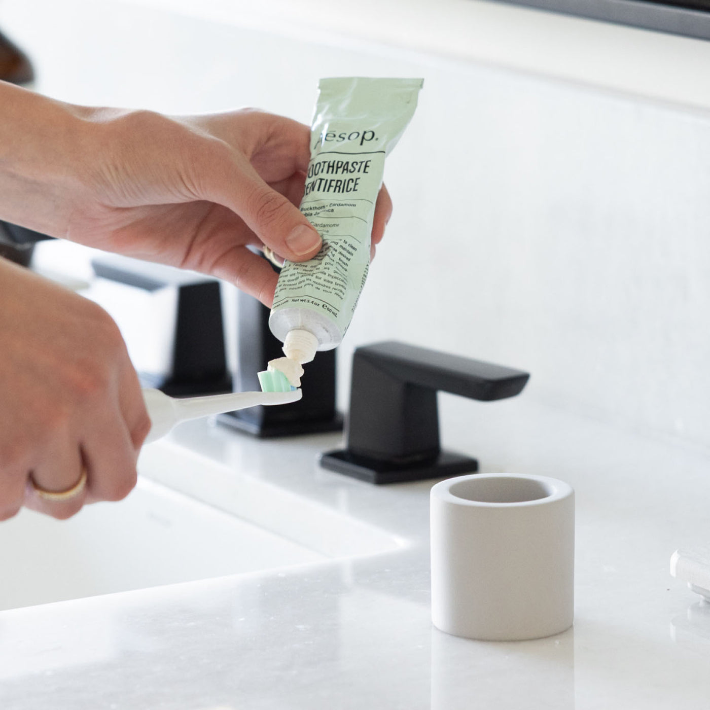 Person applying toothpaste to electric toothbrush with stone toothbrush holder sitting on a bathroom counter