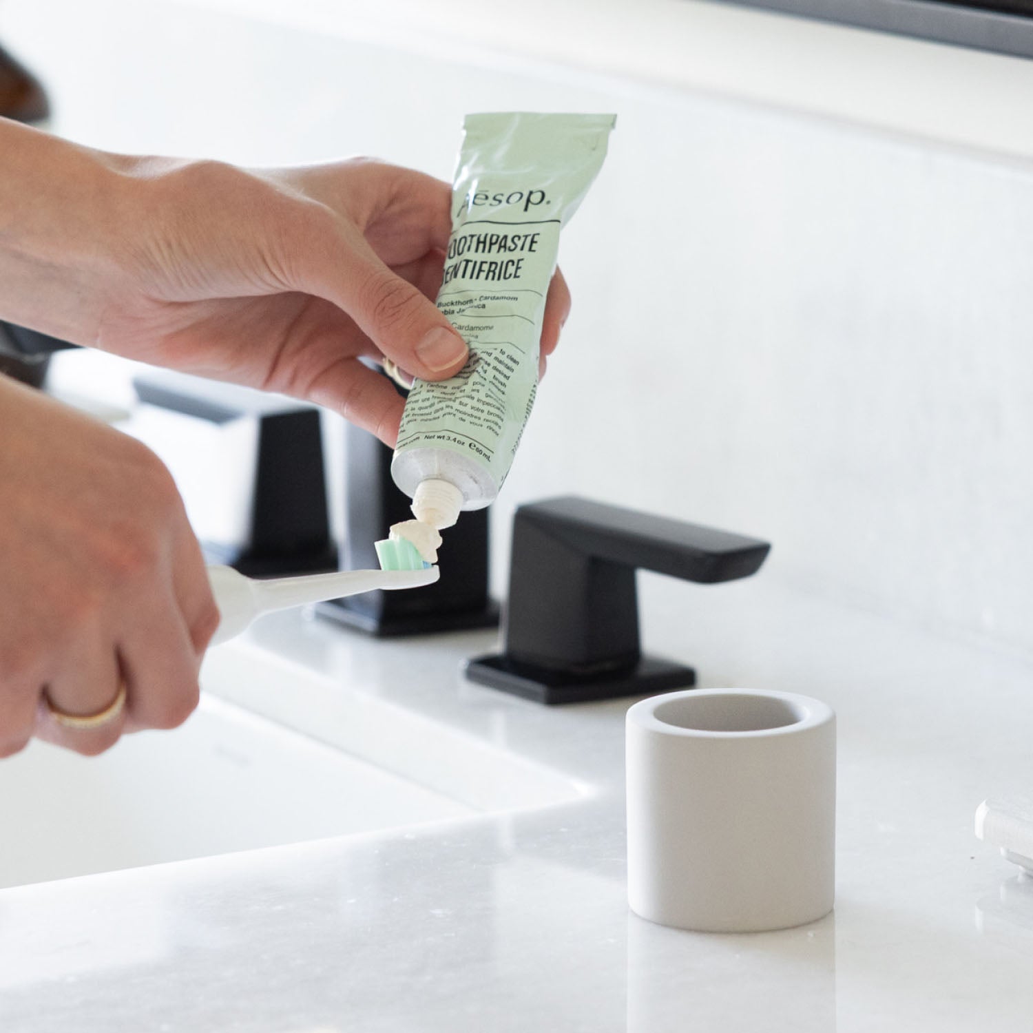 Person applying toothpaste to electric toothbrush with stone toothbrush holder sitting on a bathroom counter