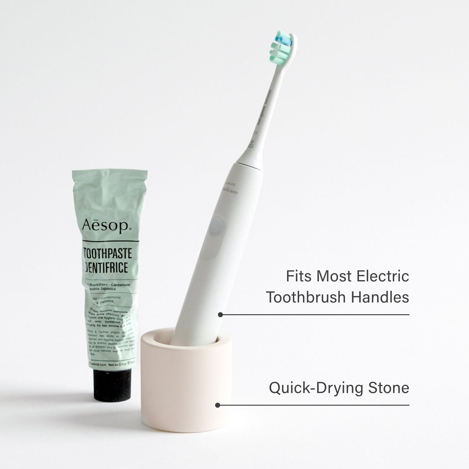 Electric toothbrush in a stone toothbrush holder next to toothpaste with product feature text