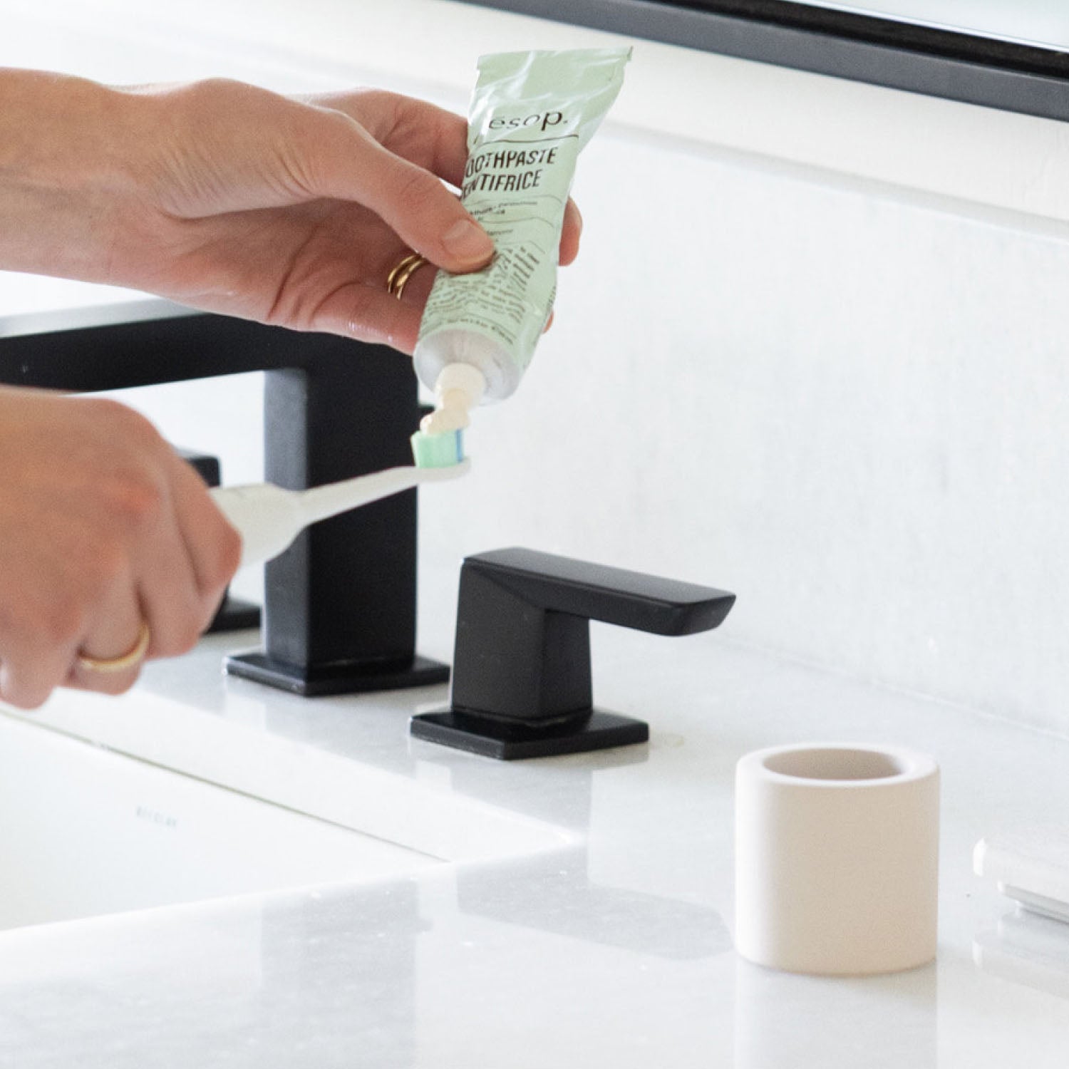 Person applying toothpaste to electric toothbrush with stone toothbrush holder sitting on a bathroom counter