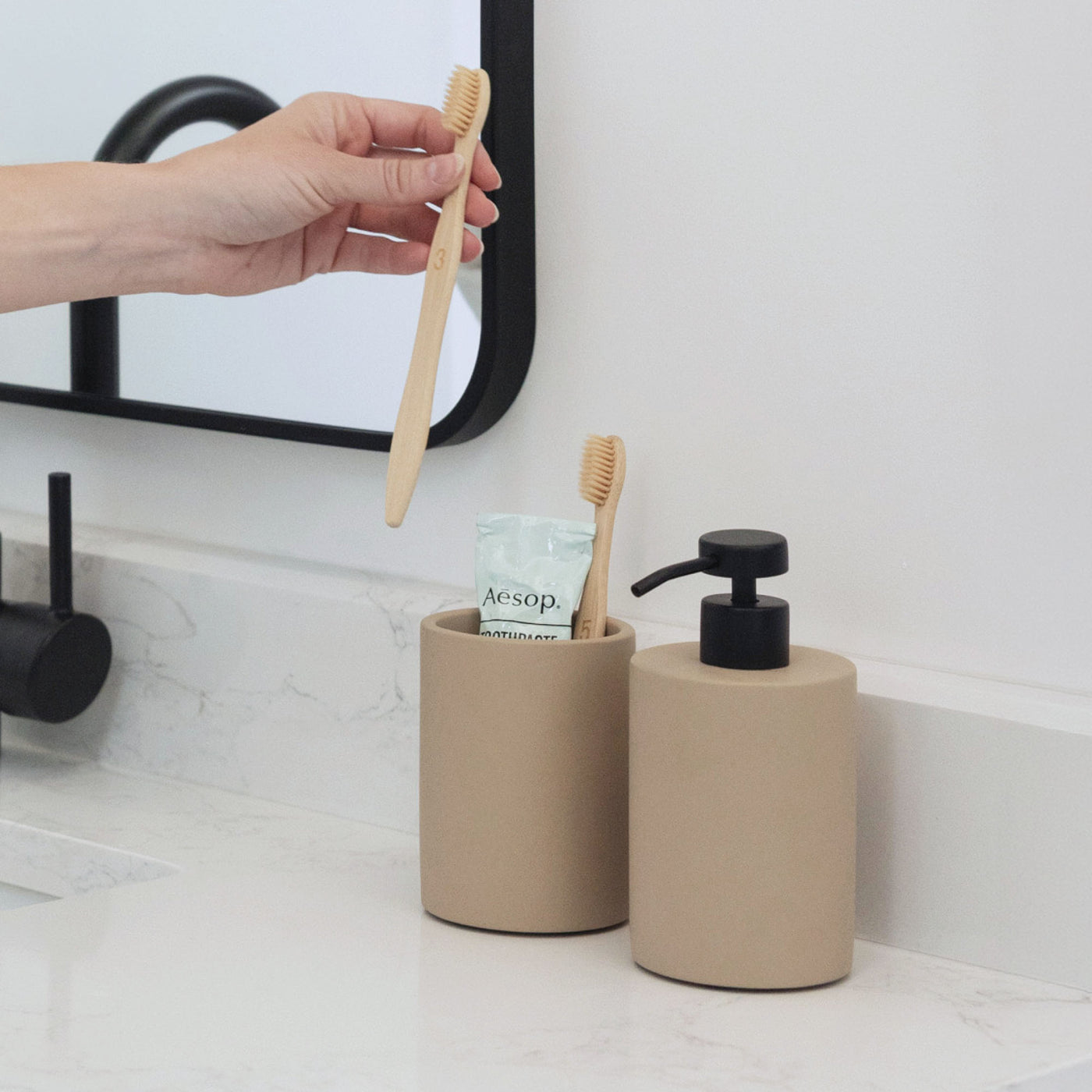 Taupe brush holder and soap dispenser with tooth brush and toothpaste.