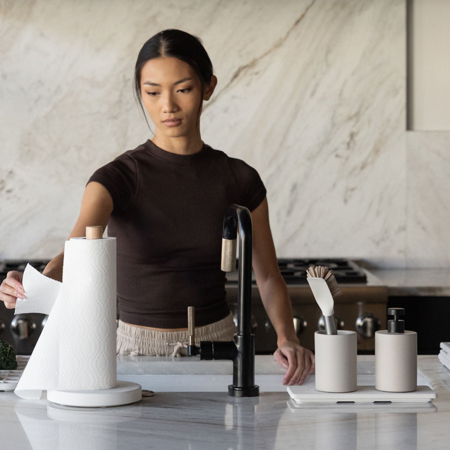 Woman standing at a kitchen counter with paper towel holder, faucet, and soap dispenser.