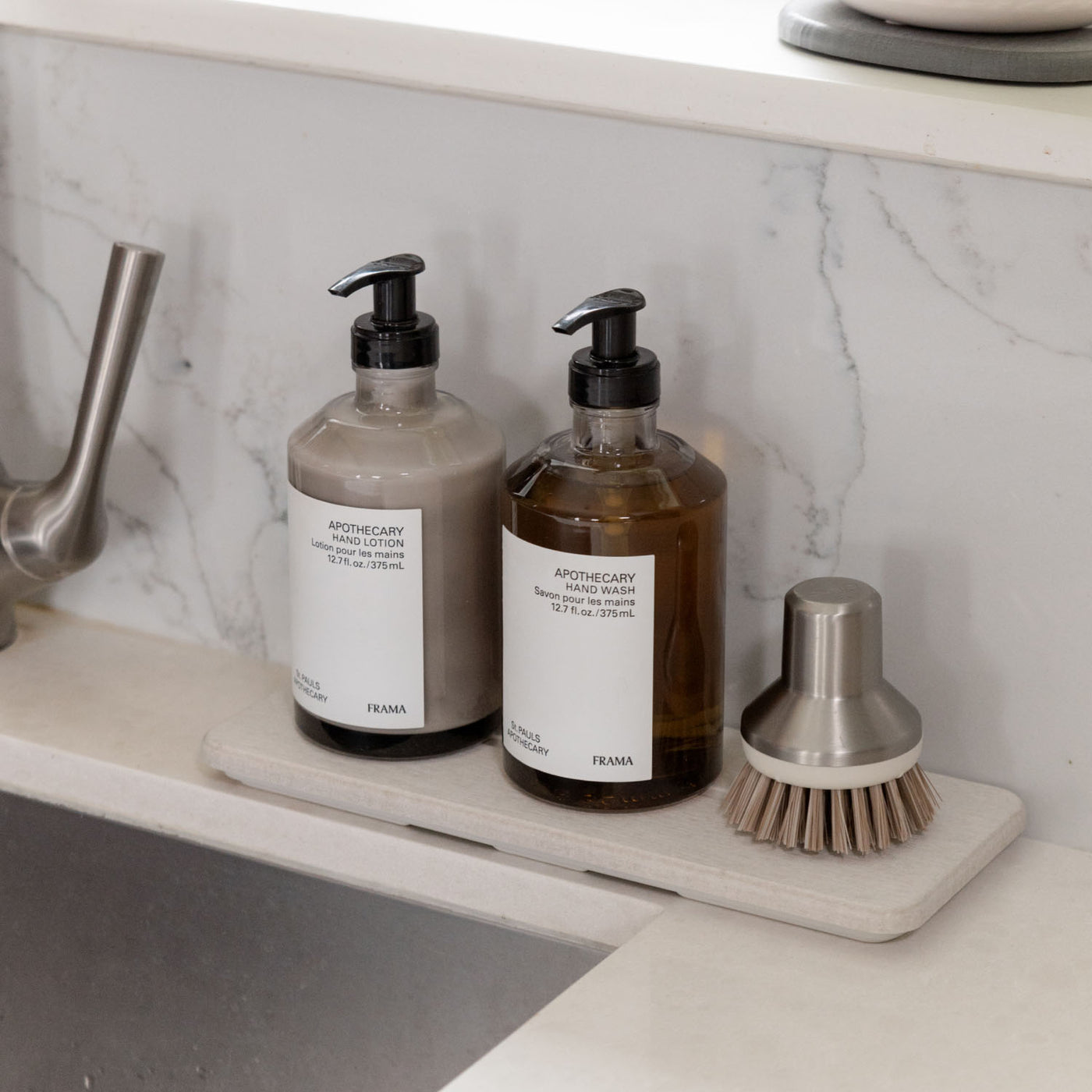 Two bottles of hand wash and a brush on stone sink caddy on a marble countertop.