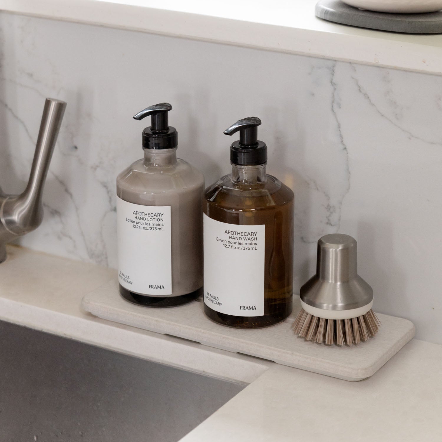 Two bottles of hand wash and a brush on stone sink caddy on a marble countertop.