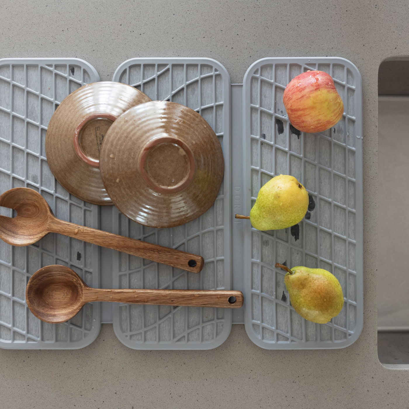 light grey Drying mat with ceramic plates, wooden spoons, and fruits on a kitchen counter.