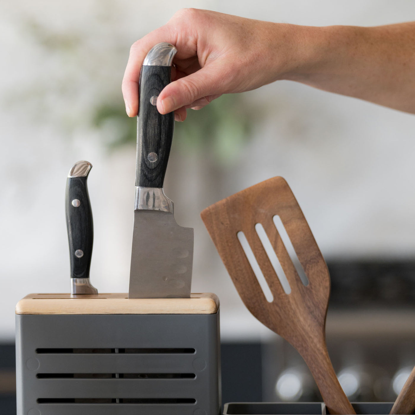 Hand holding a knife above a knife block with a wooden spatula in dish drying rack