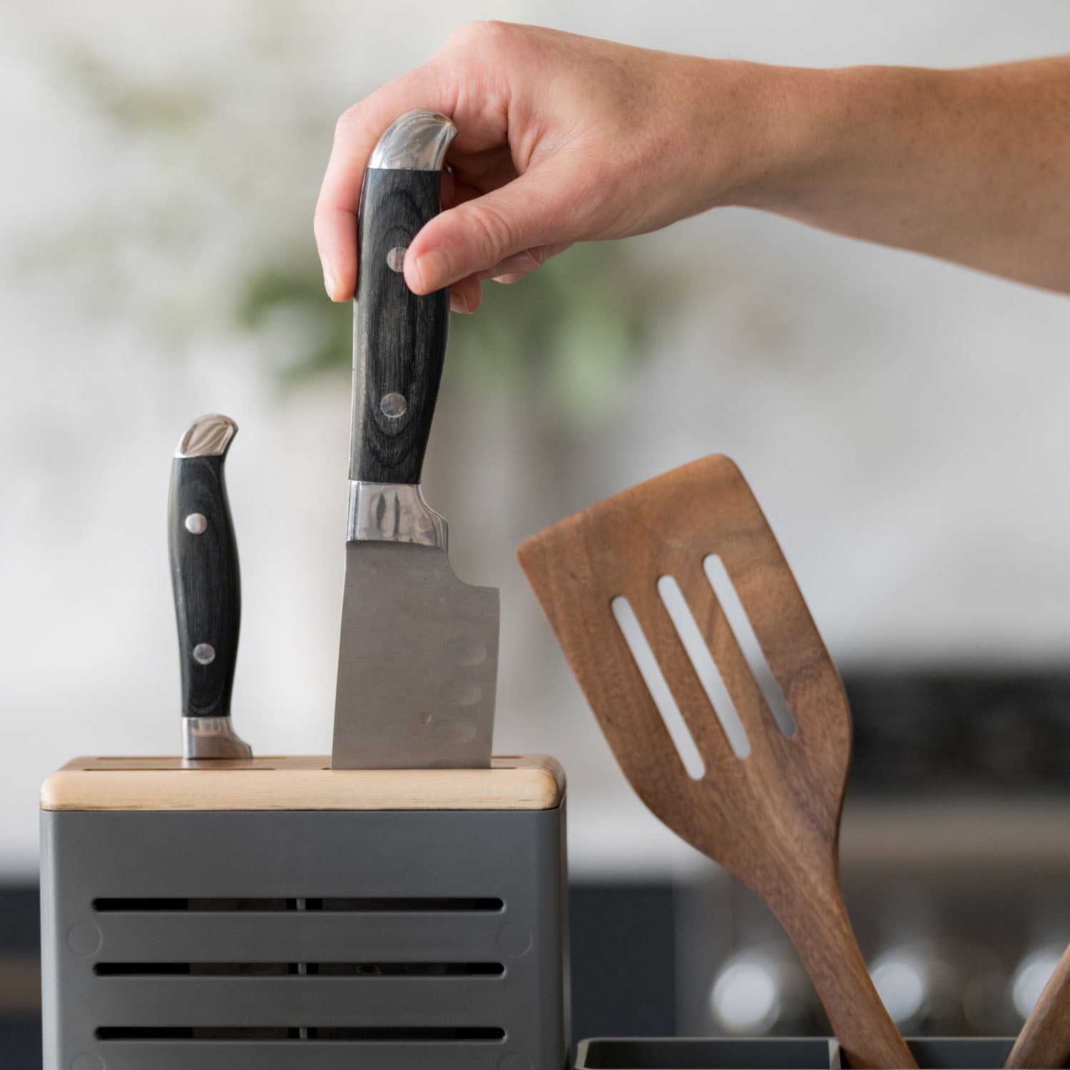 Hand holding a knife above a knife block with a wooden spatula in dish drying rack