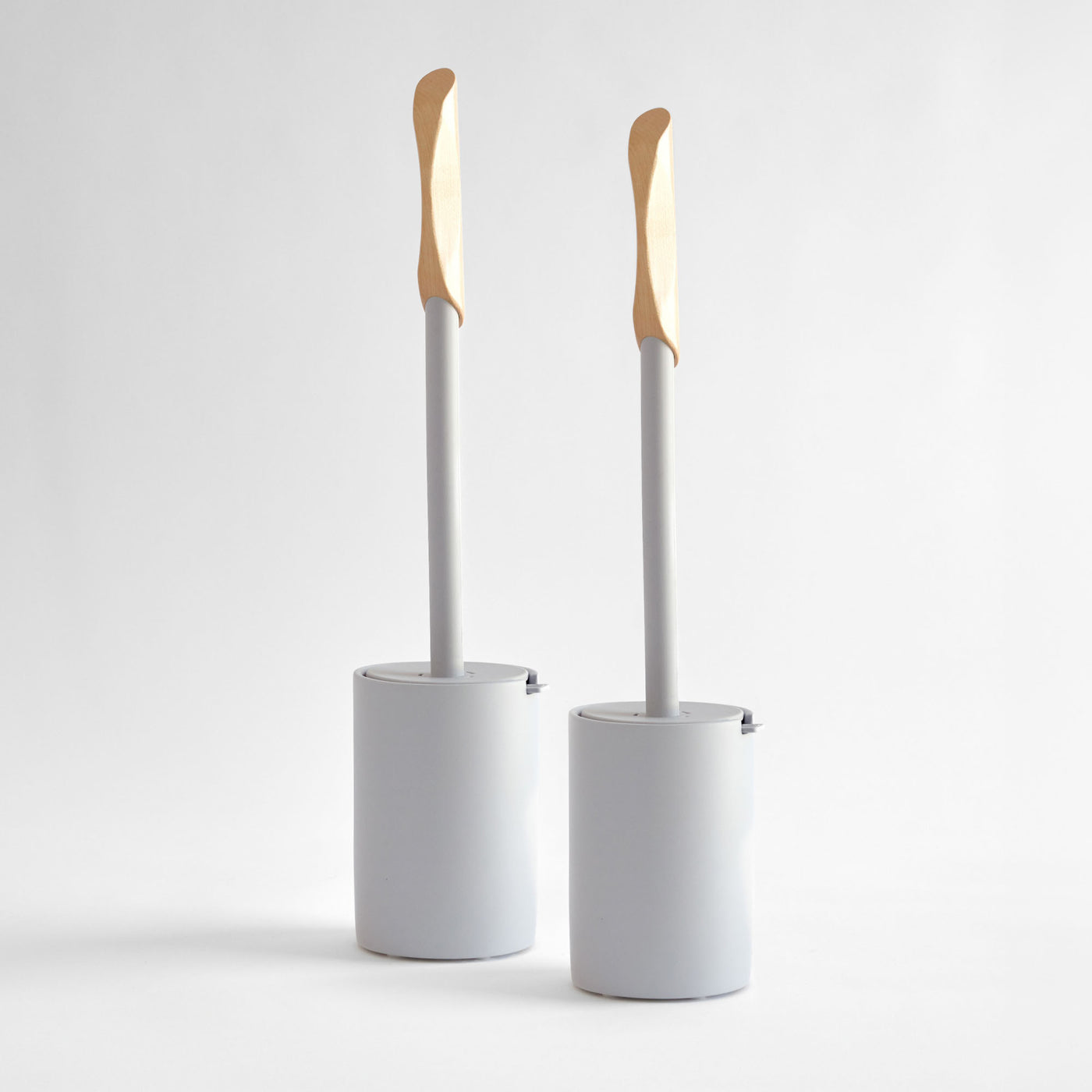 Two modern, white toilet brushes with wood handle. 