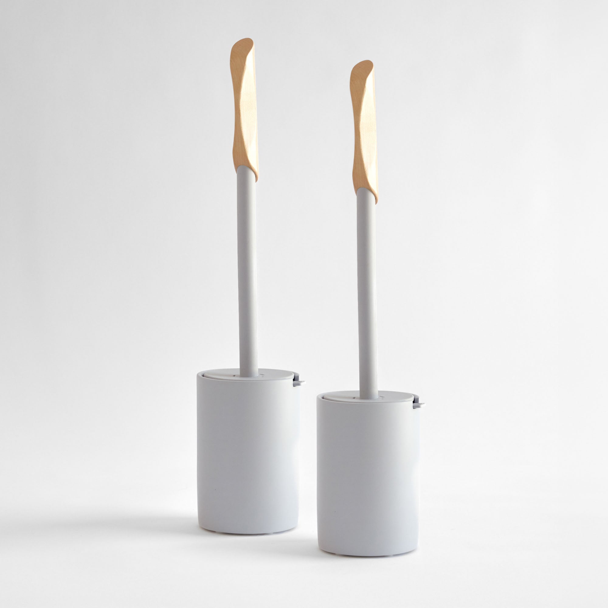 Two modern, white toilet brushes with wood handle. 