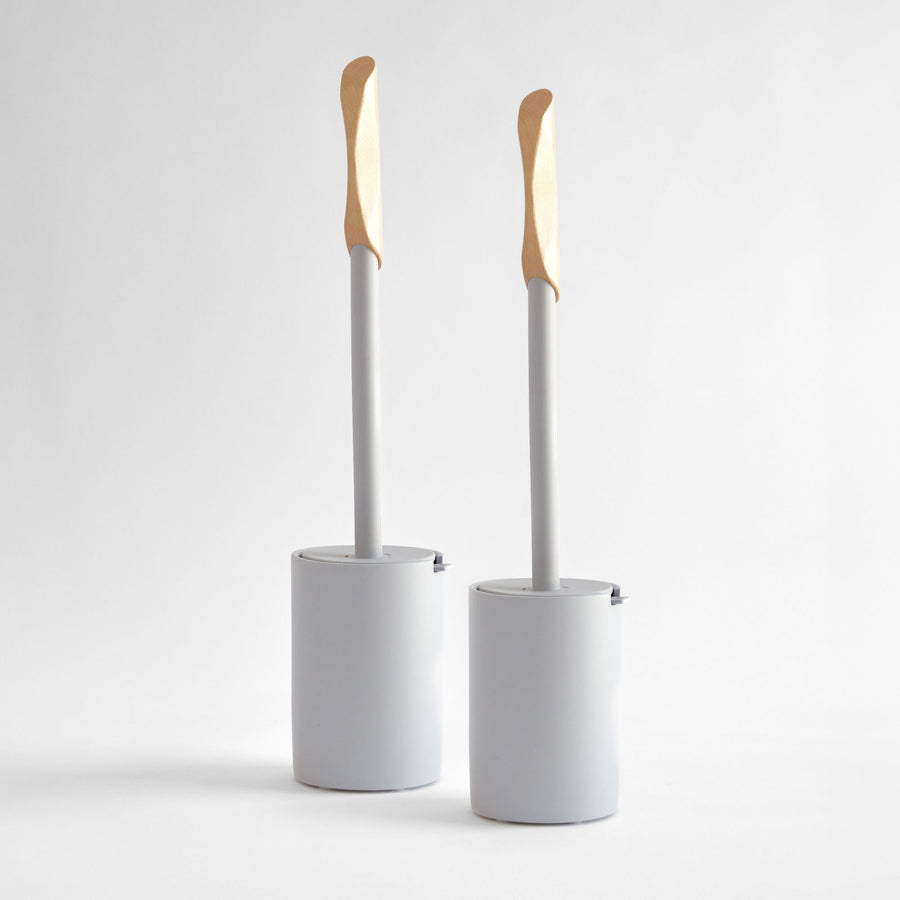 Two modern, white toilet brushes with wood handle. 