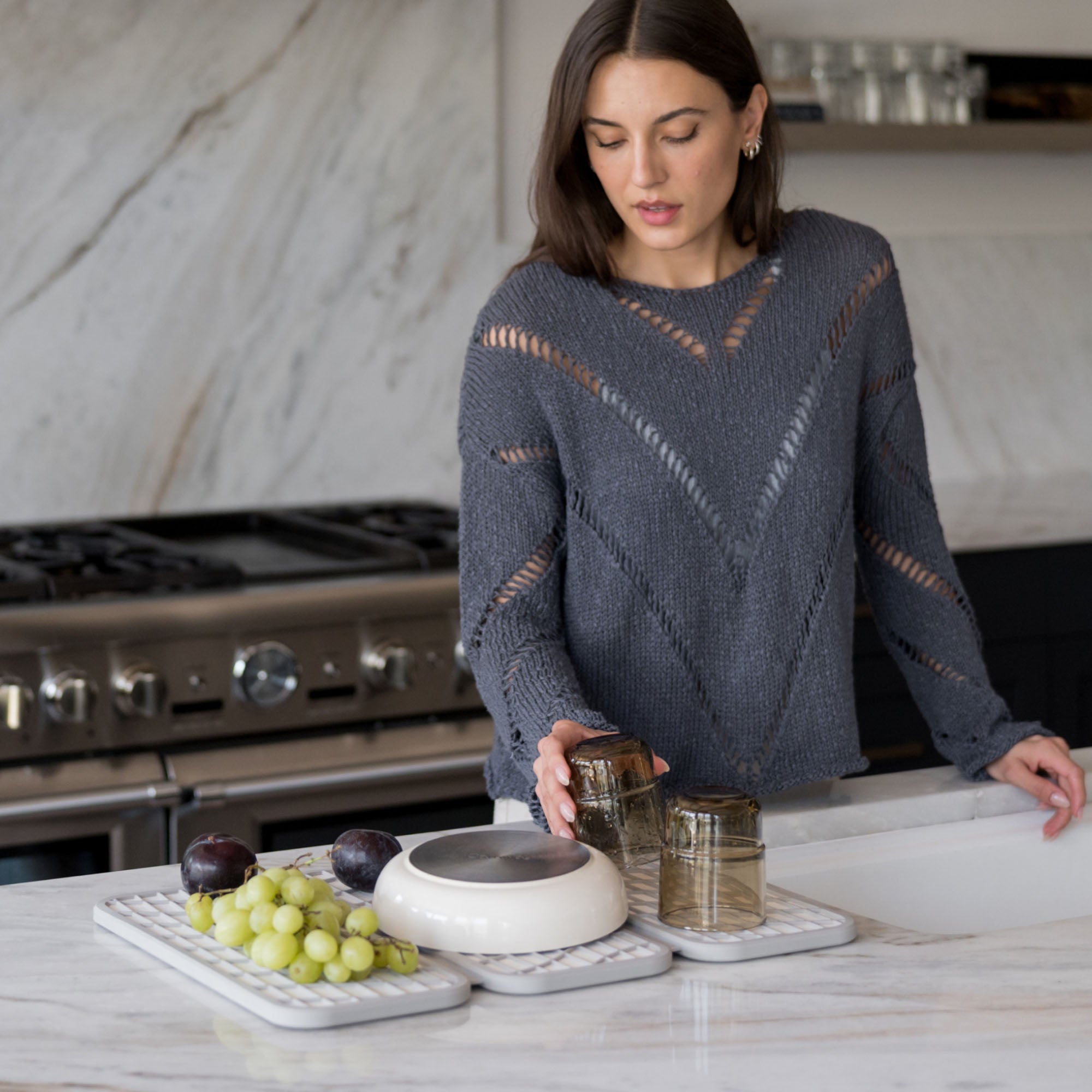 Woman with Drift Sandstone Dish Pad with produce, pots, and glasses on it in beautiful kitchen.