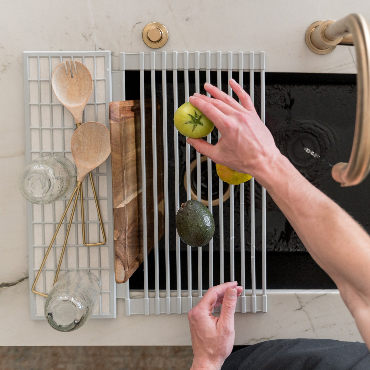 Person placing a tomato on an over the sink dish pad with various kitchen items drying on the pad