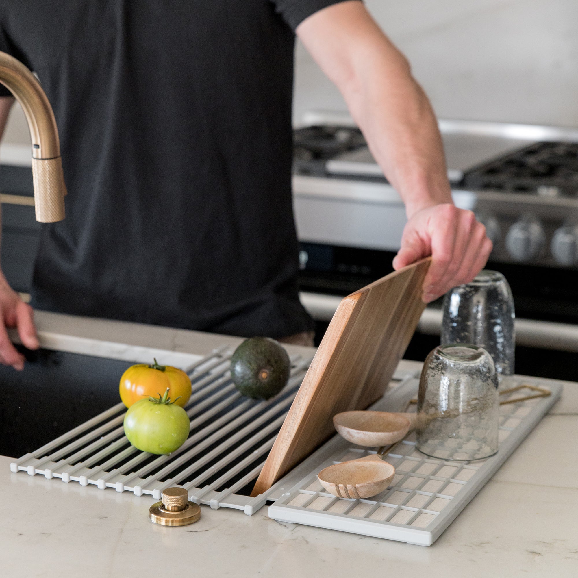 Person placing cutting board into an over the sink dish pad with fruits and kitchen utensils on a countertop on the pad