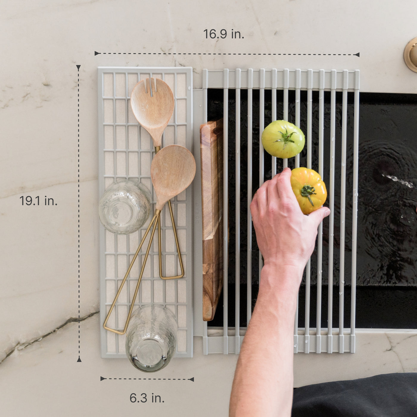 Person placing a tomato on an over the sink dish pad with various kitchen items drying on the pad with measurements overlaid