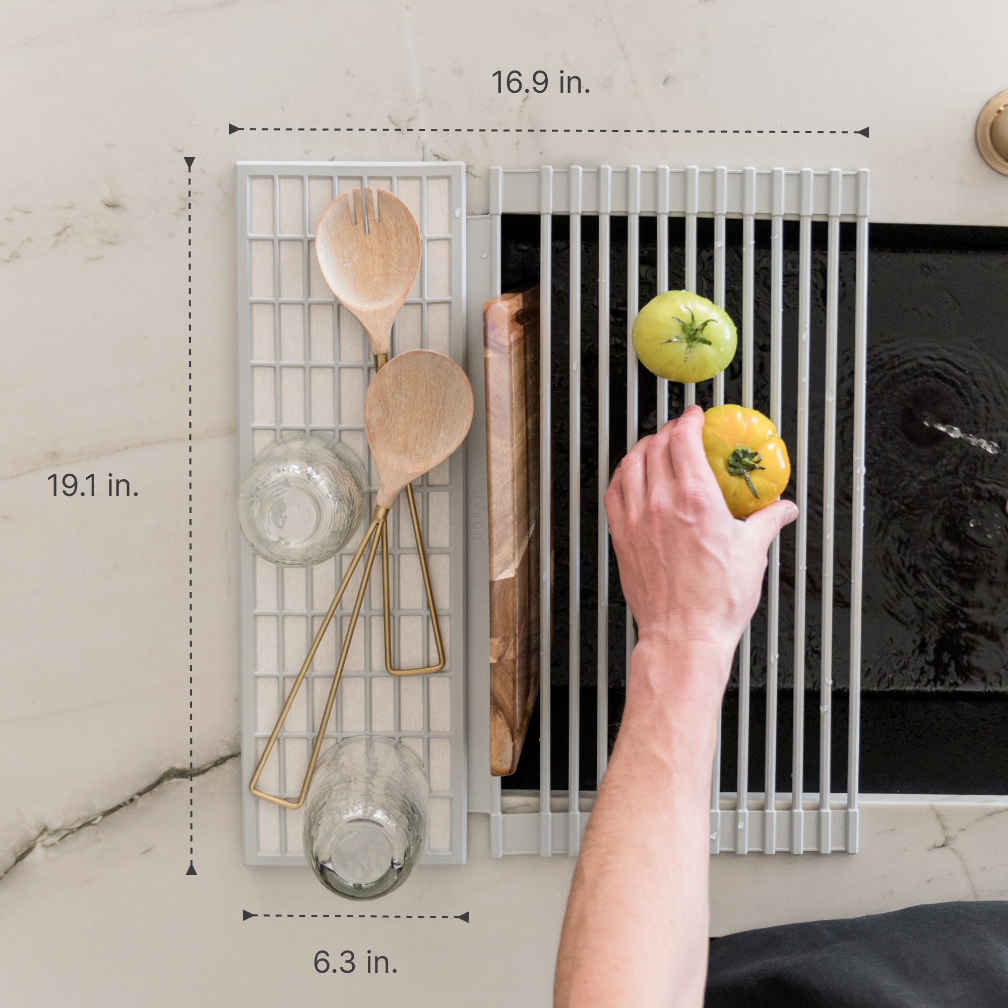 Person placing a tomato on an over the sink dish pad with various kitchen items drying on the pad with measurements overlaid
