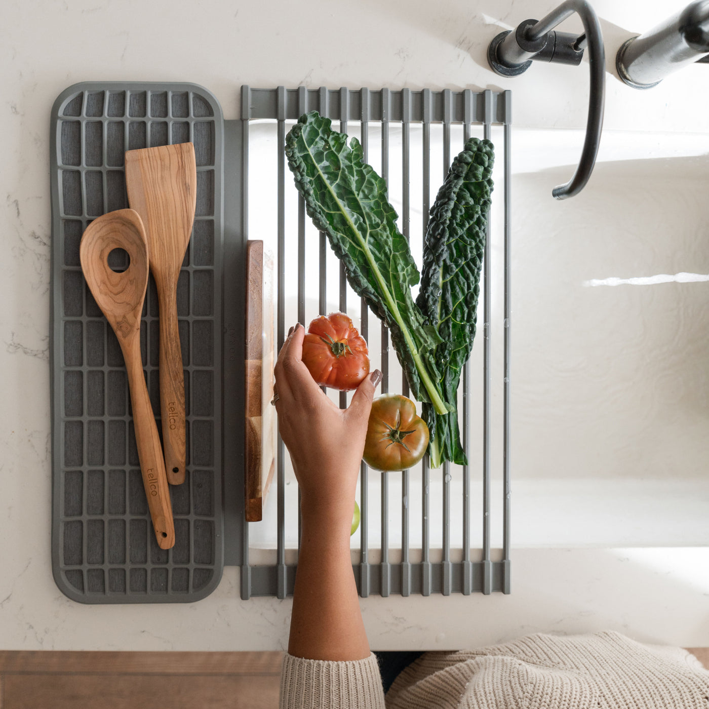 Person placing a tomato on an over the sink dish pad with various kitchen items drying on the pad