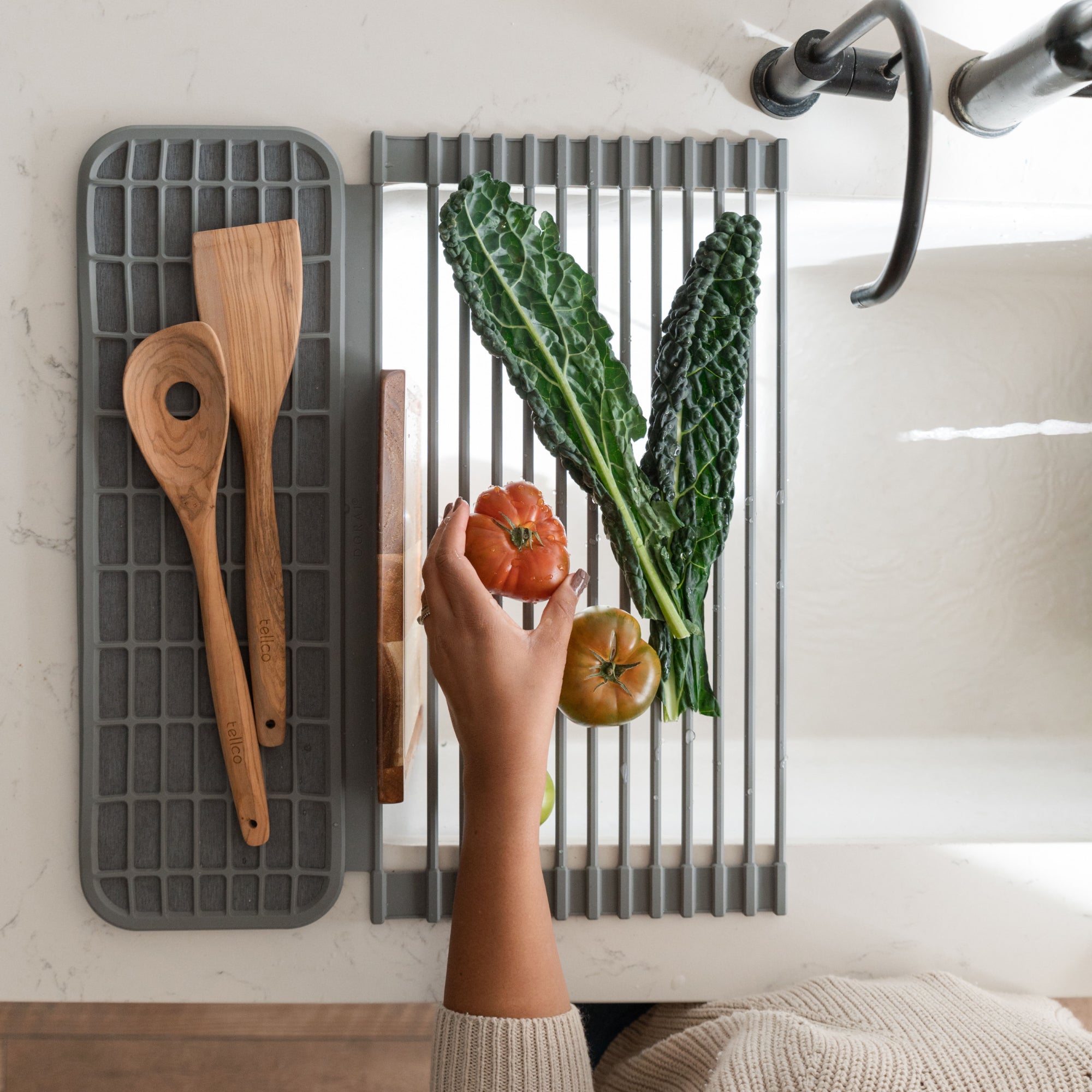 Person placing a tomato on an over the sink dish pad with various kitchen items drying on the pad