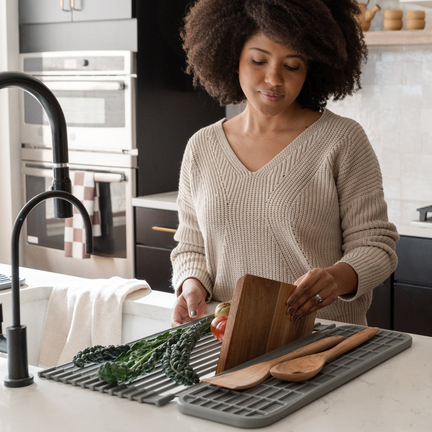 Person placing cutting board into an over the sink dish pad with vegatables and kitchen utensils on a countertop on the pad
