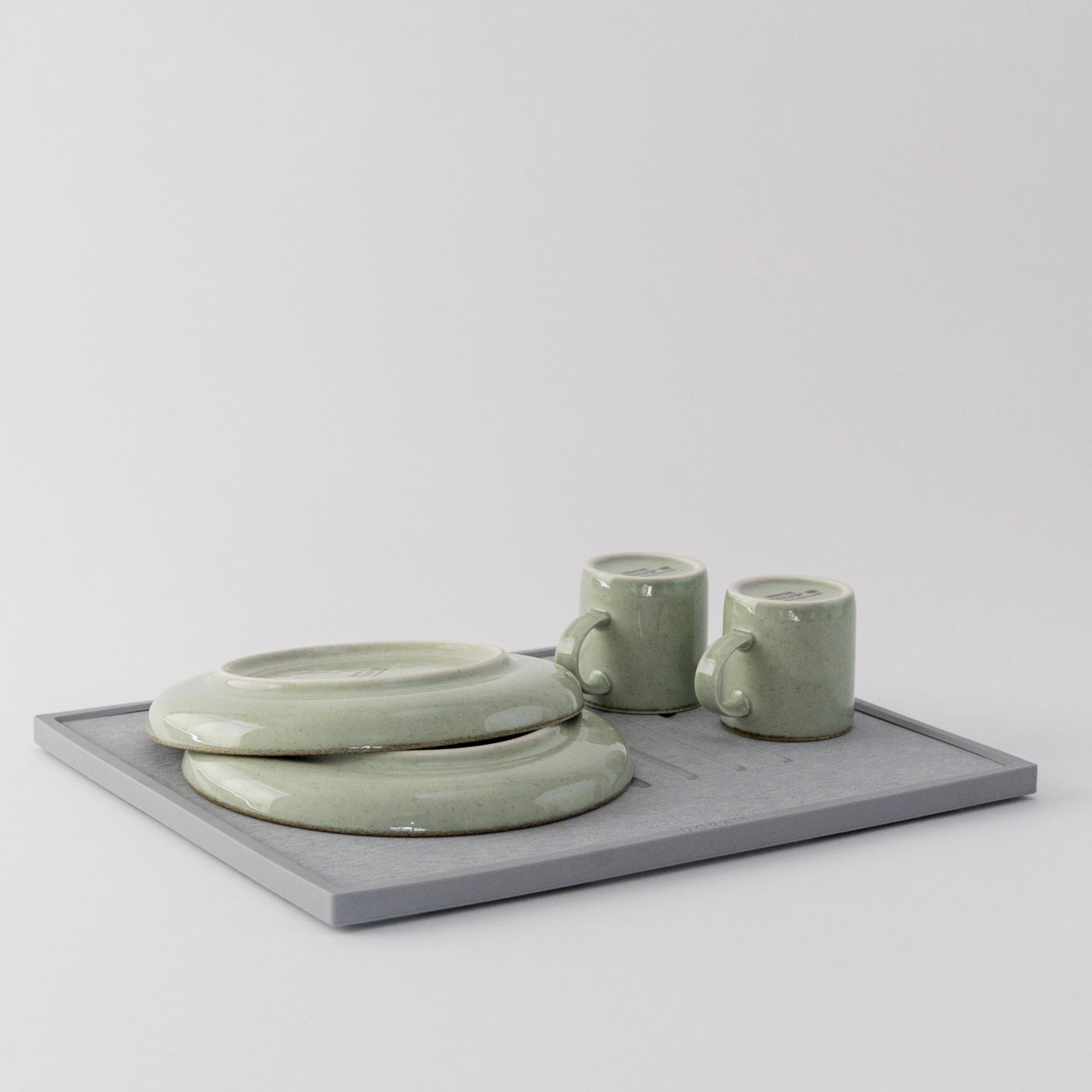 Set of green ceramic items including a bowl, two mugs, and a quick drying dish pad on a light gray background