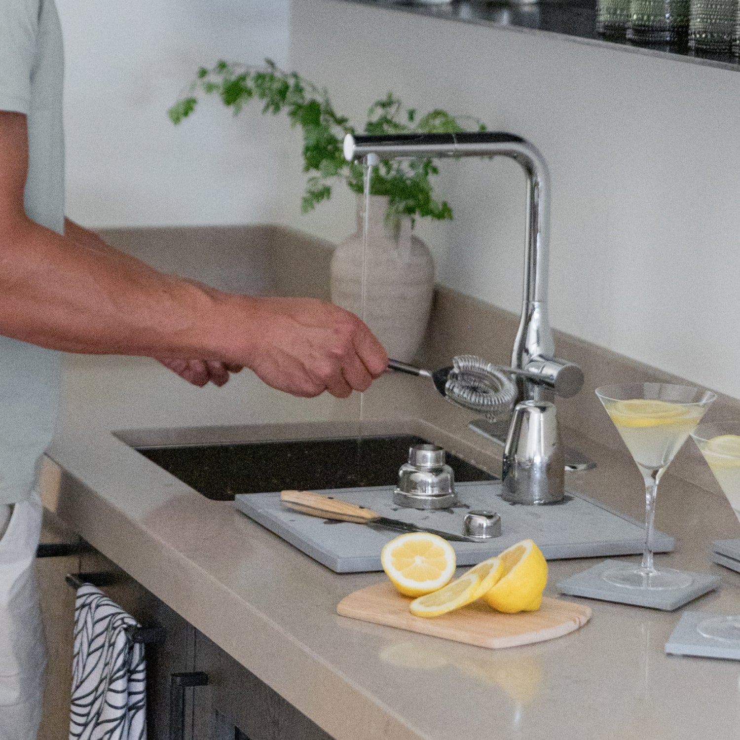Person preparing a drink in a kitchen with lemons and a drying stone on the counter.