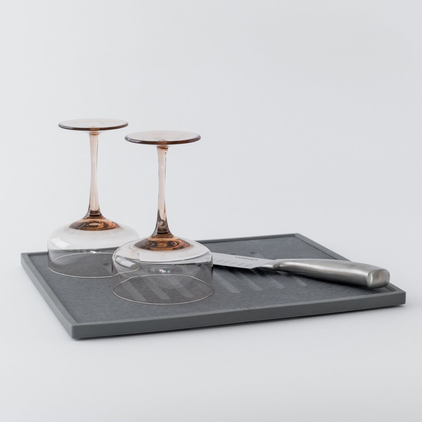 Two wine glasses on a gray dish drying stone with a knife on a light gray background