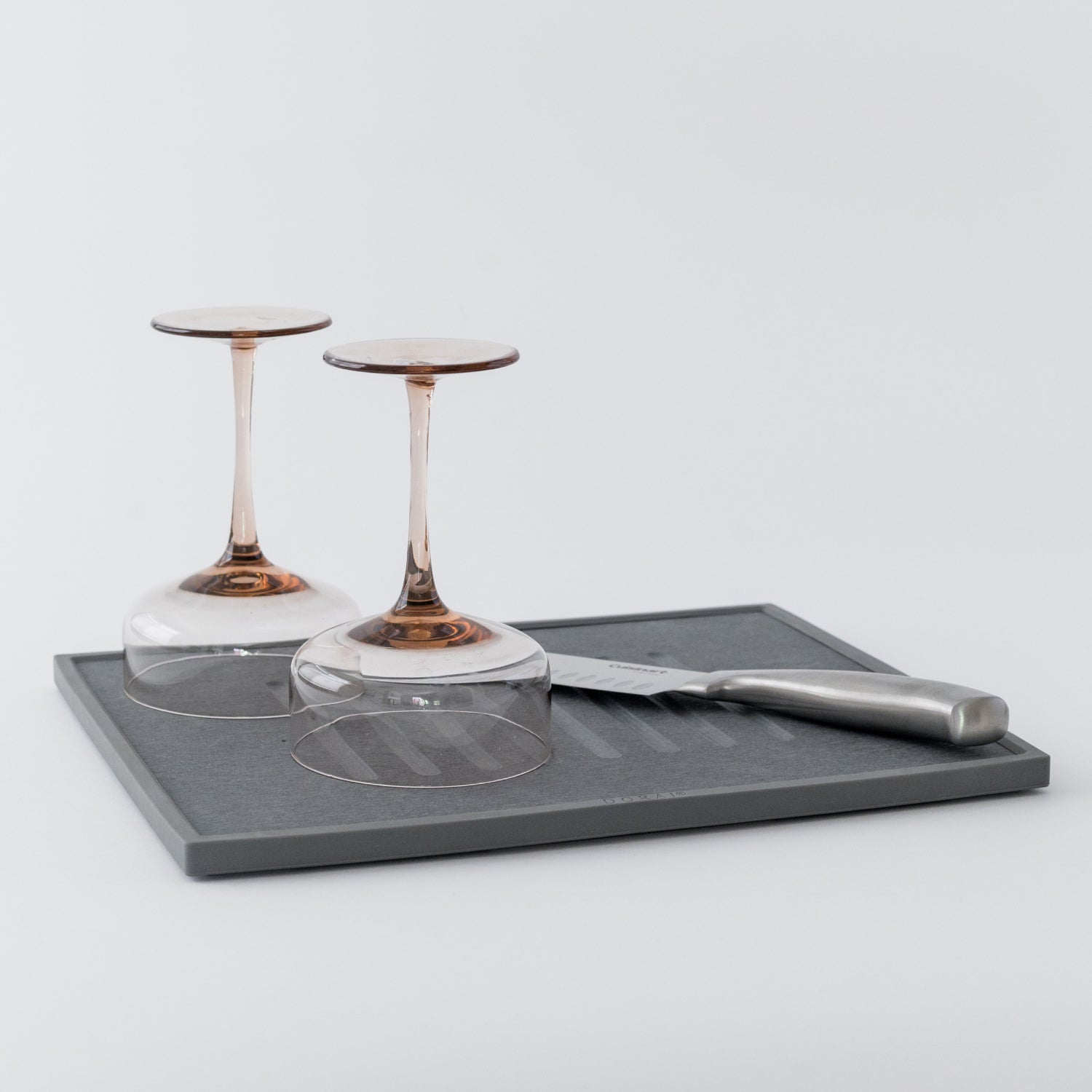 Two wine glasses on a gray dish drying stone with a knife on a light gray background