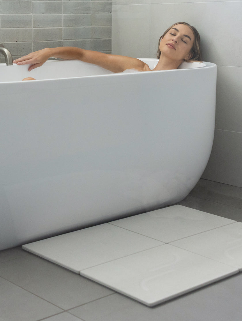Woman relaxing in large, modern bathroom with quick-drying modern bath stone. 