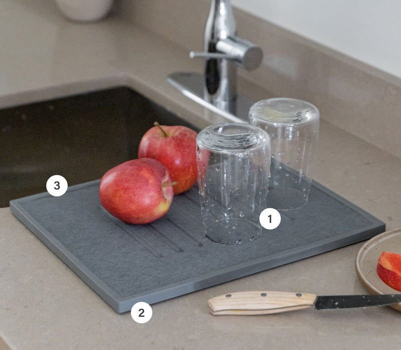 Grey dish drying stone in kitchen with glasses and produce. 
