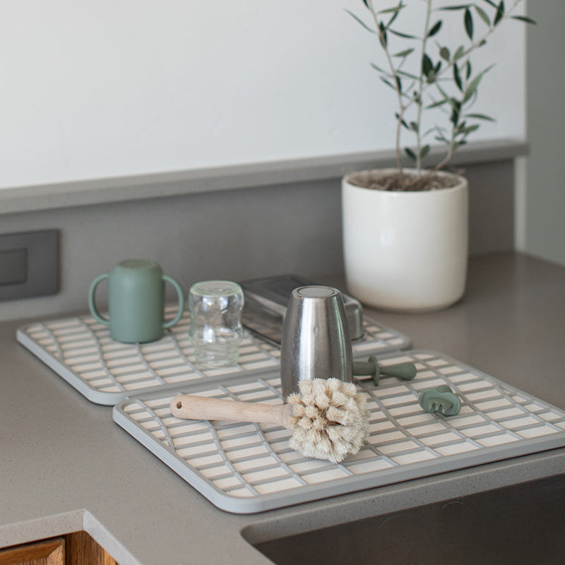 baby bottles and utensils being dried on off white dish pad with grey silicone