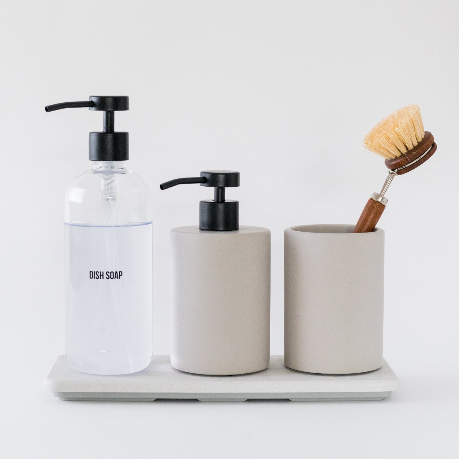Bathroom accessories including a dish soap bottle, two soap dispensers, and a scrub brush on a white surface.